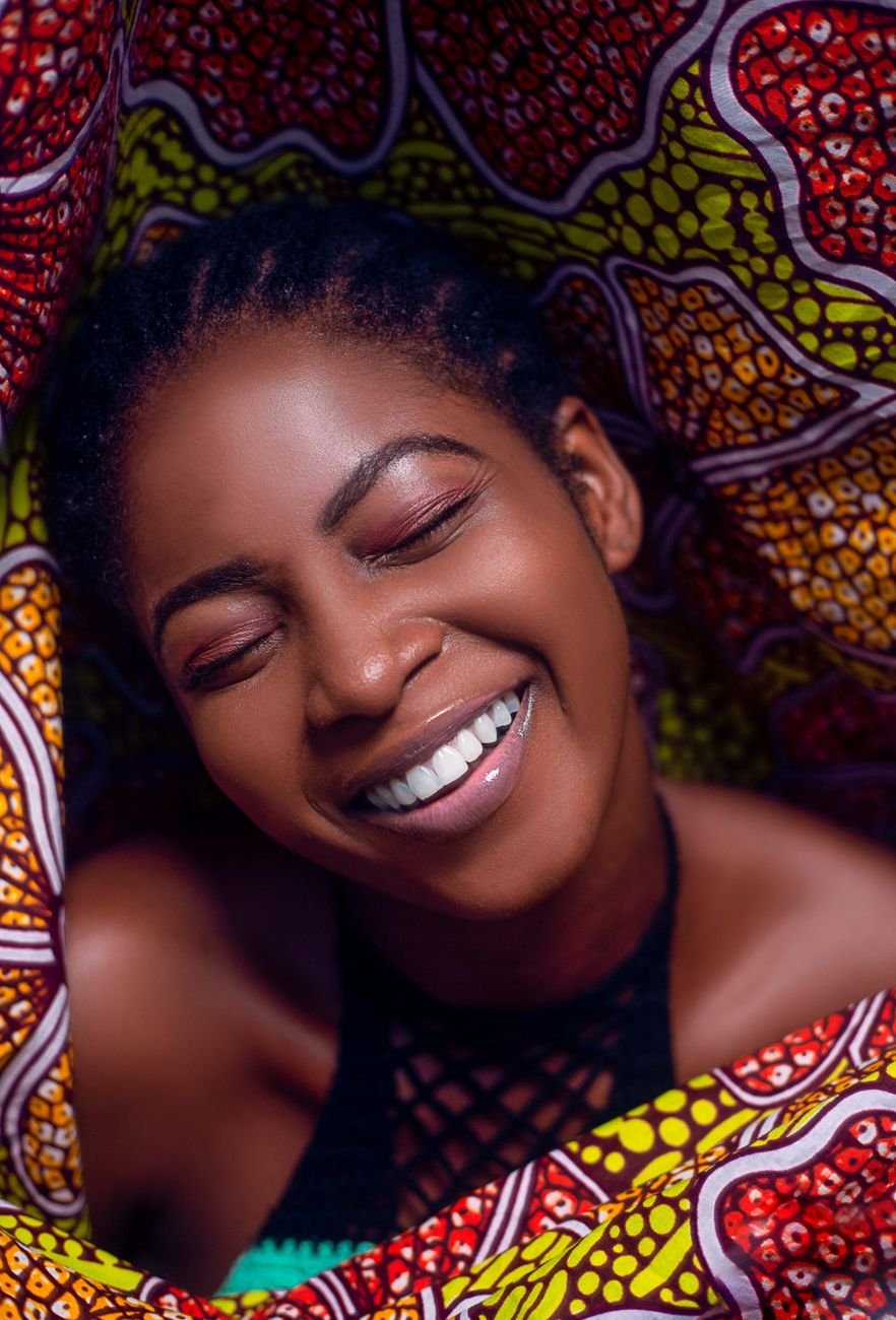 Smiling African woman surrounded by vibrant, patterned fabric in bright lighting.